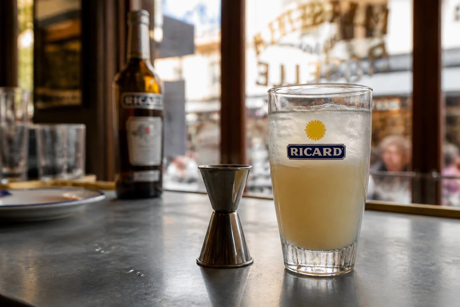 Verre de Ricard louché sur un comptoir de bar français avec un jigger de mesure de 2 cl posé à côté