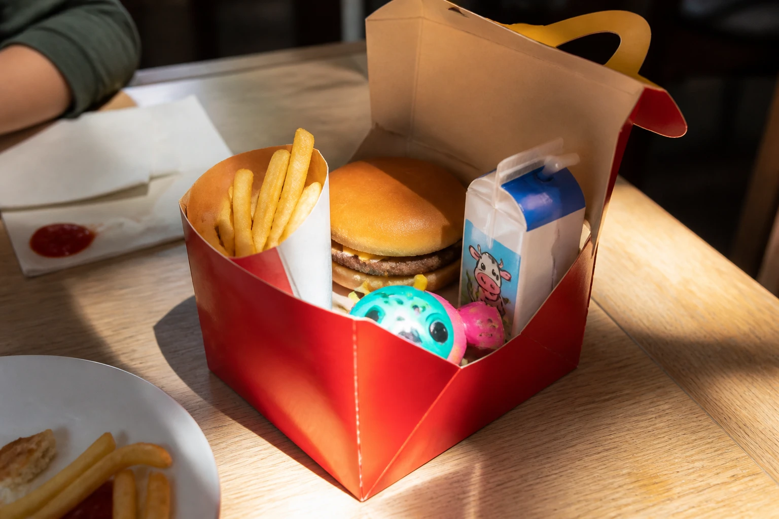 Happy Meal McDonald's ouvert sur une table en bois avec hamburger, frites, lait et jouet